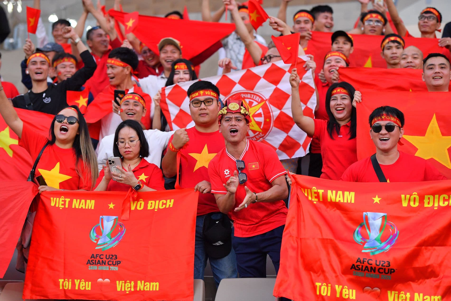 Người hâm mộ U23 Việt Nam trên khán đài cổ vũ, giơ cao cờ và biểu ngữ 'Việt Nam Vô Địch', thể hiện kỳ vọng lớn lao.