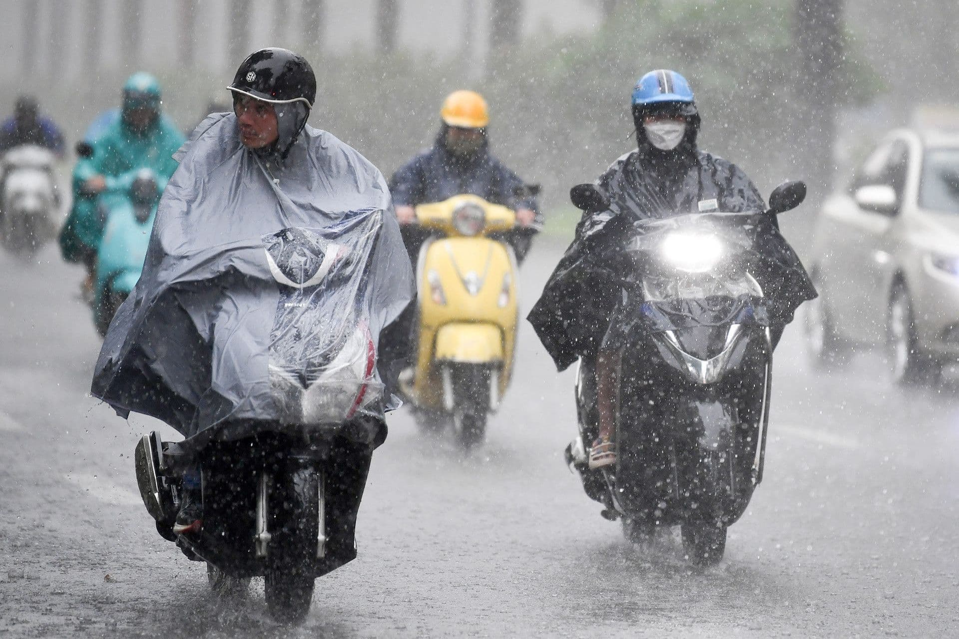 Người đi xe máy đội mưa lớn trên đường phố Hà Nội, minh họa sự chuyển mình kịch tính của thời tiết từ nắng sang giông.