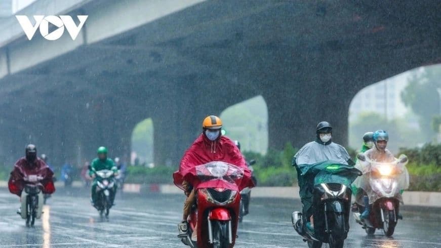 Người đi xe máy đội áo mưa trên đường phố Hà Nội trong cơn mưa lớn, thể hiện sự ảnh hưởng của thời tiết đến cuộc sống hàng ngày.