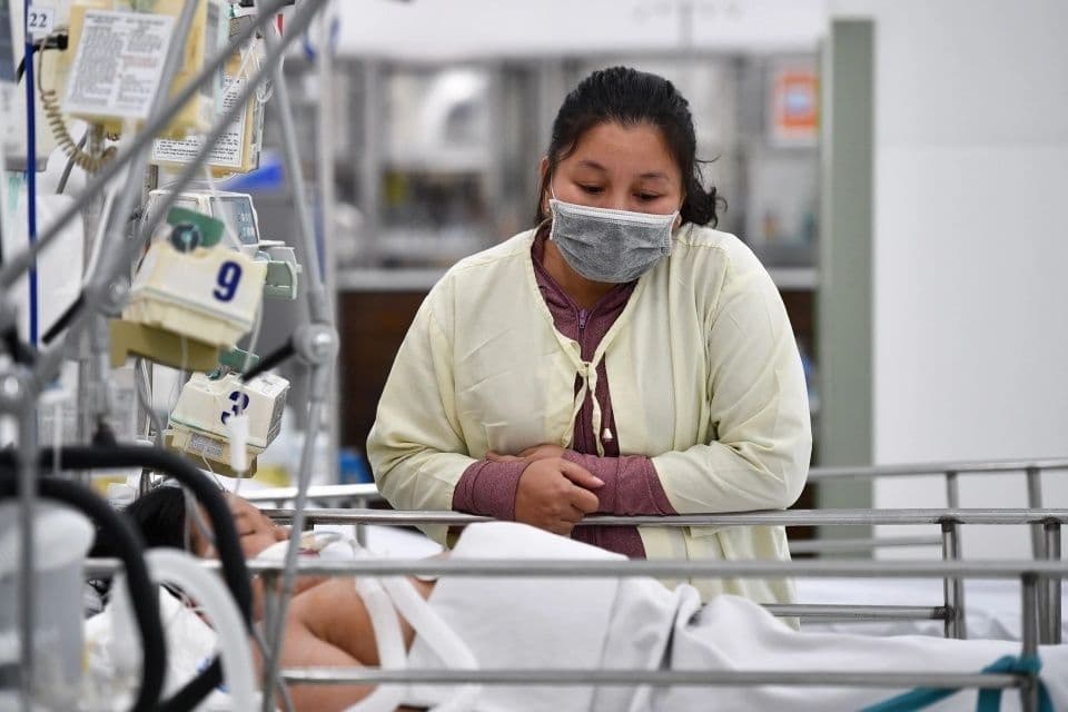 Người mẹ lo lắng nhìn con nằm trong phòng hồi sức tích cực với máy móc hỗ trợ, minh họa biến chứng nặng của tay chân miệng EV71