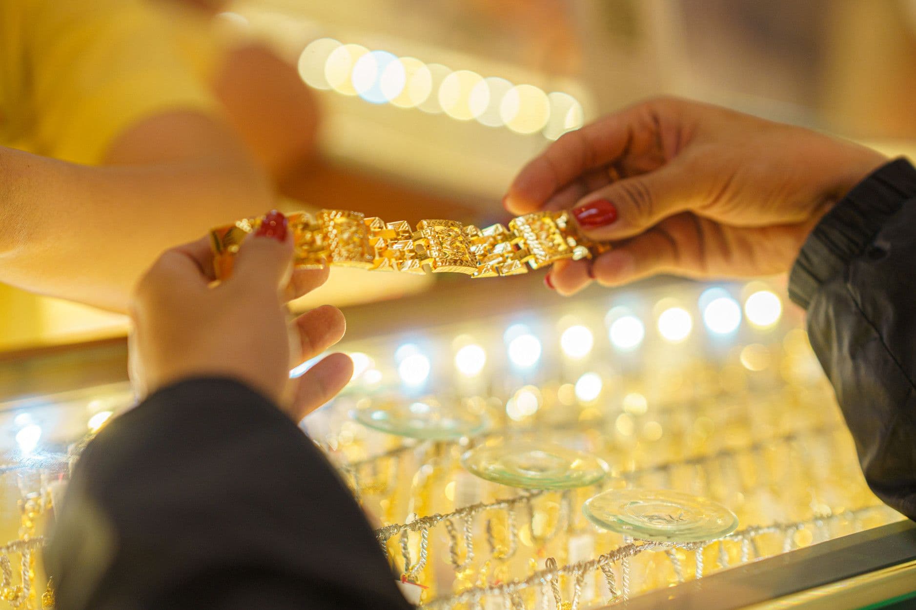 Người mua và người bán trao đổi vòng vàng tại cửa hàng, thể hiện giao dịch và giá trị của vàng trên thị trường.