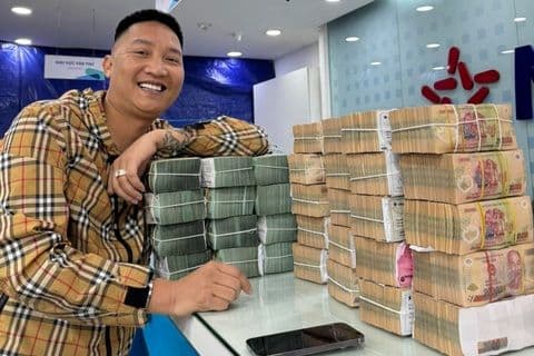 Người đàn ông mỉm cười bên các cọc tiền Việt Nam, tượng trưng cho tác động tài chính của giá xăng dầu lên mỗi gia đình