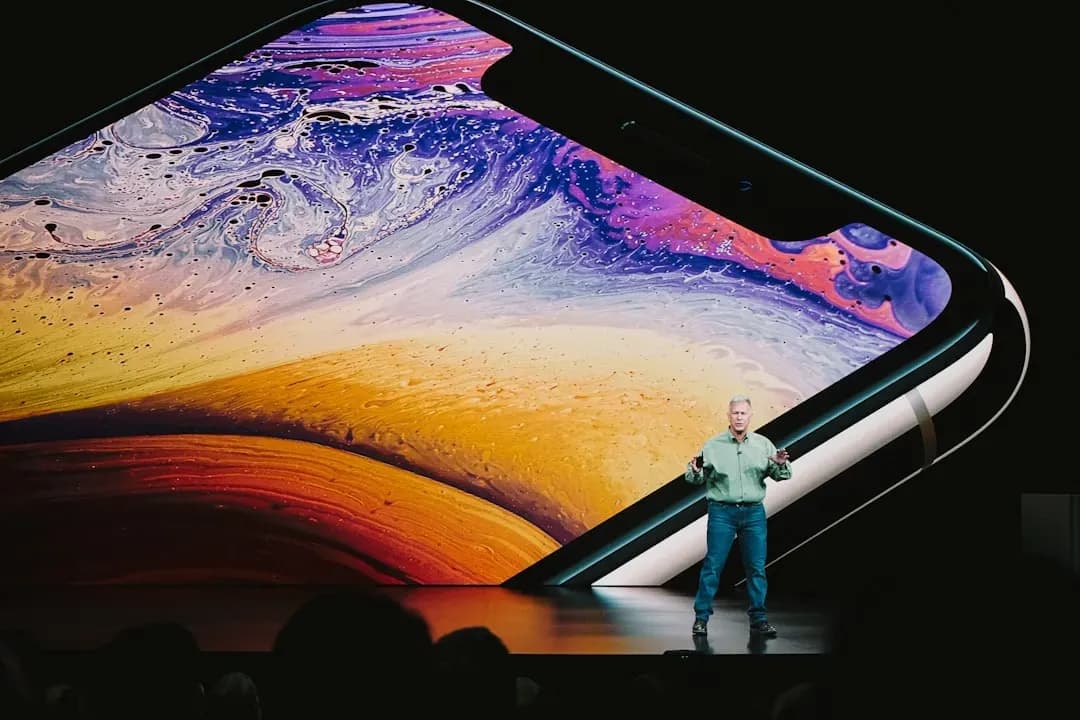 Người đàn ông thuyết trình trước màn hình lớn hiển thị giao diện iPhone, tượng trưng cho tầm nhìn và tương lai của biểu tượng công nghệ.