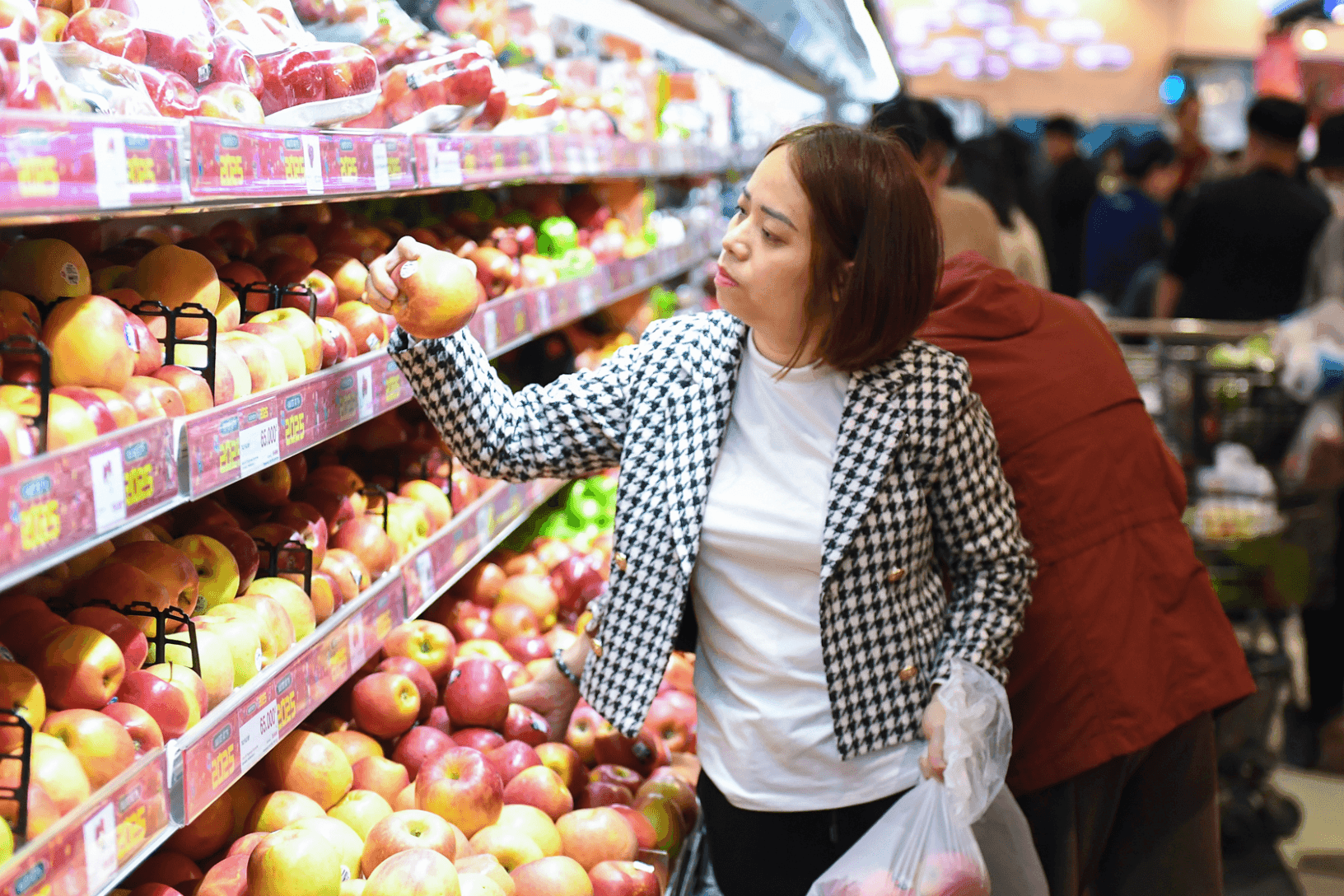 Người phụ nữ đang chọn mua táo trong siêu thị, minh họa tác động của giá xăng tăng lên chi tiêu hàng ngày của người tiêu dùng.