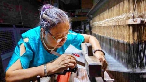 Người phụ nữ cao tuổi đang dệt vải trên khung cửi, tượng trưng cho sự đóng góp của người lớn tuổi vào nền kinh tế bạc.