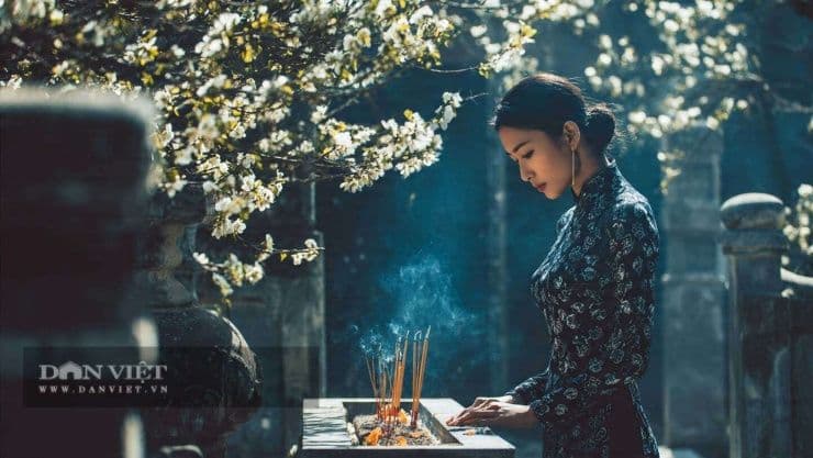 Người phụ nữ mặc áo dài thắp hương tại mộ phần trong tiết Thanh Minh.