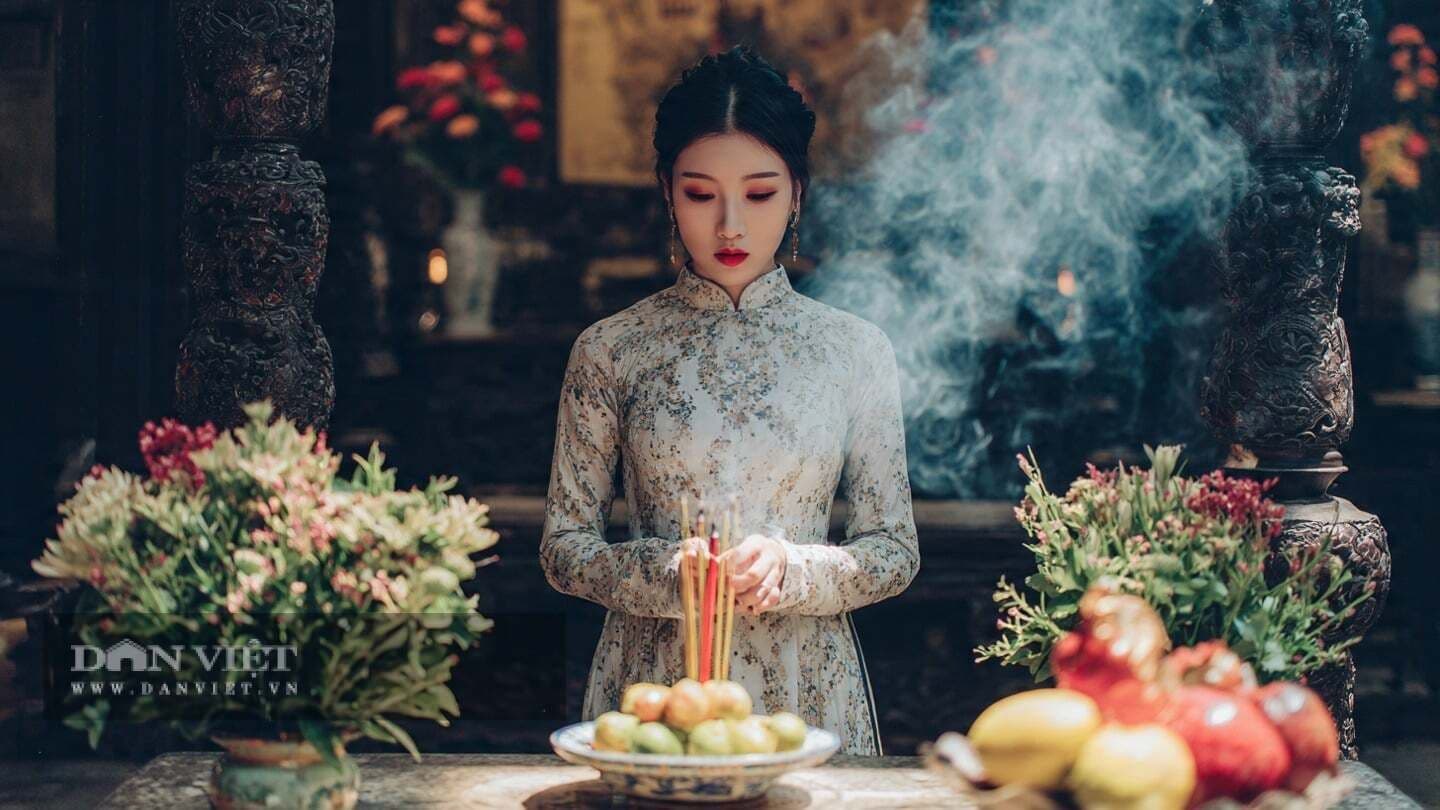 Người phụ nữ mặc áo dài truyền thống thành kính thắp hương trước bàn thờ, thể hiện việc giữ gìn nét đẹp cổ truyền.