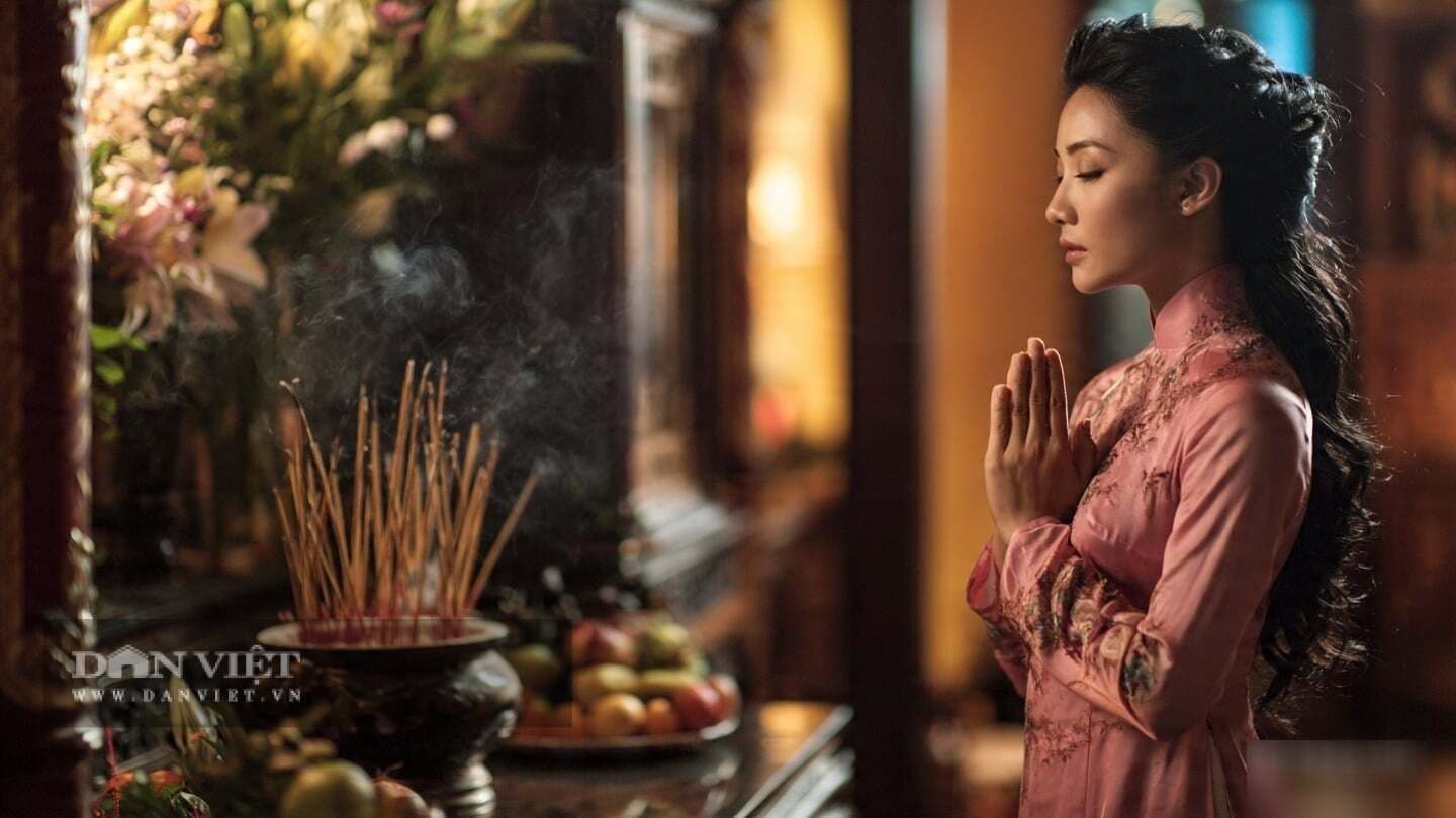 Người phụ nữ thành tâm chắp tay cầu nguyện trước bàn thờ với khói hương nghi ngút, tượng trưng cho sự thành kính trong ngày Rằm tháng Tư.