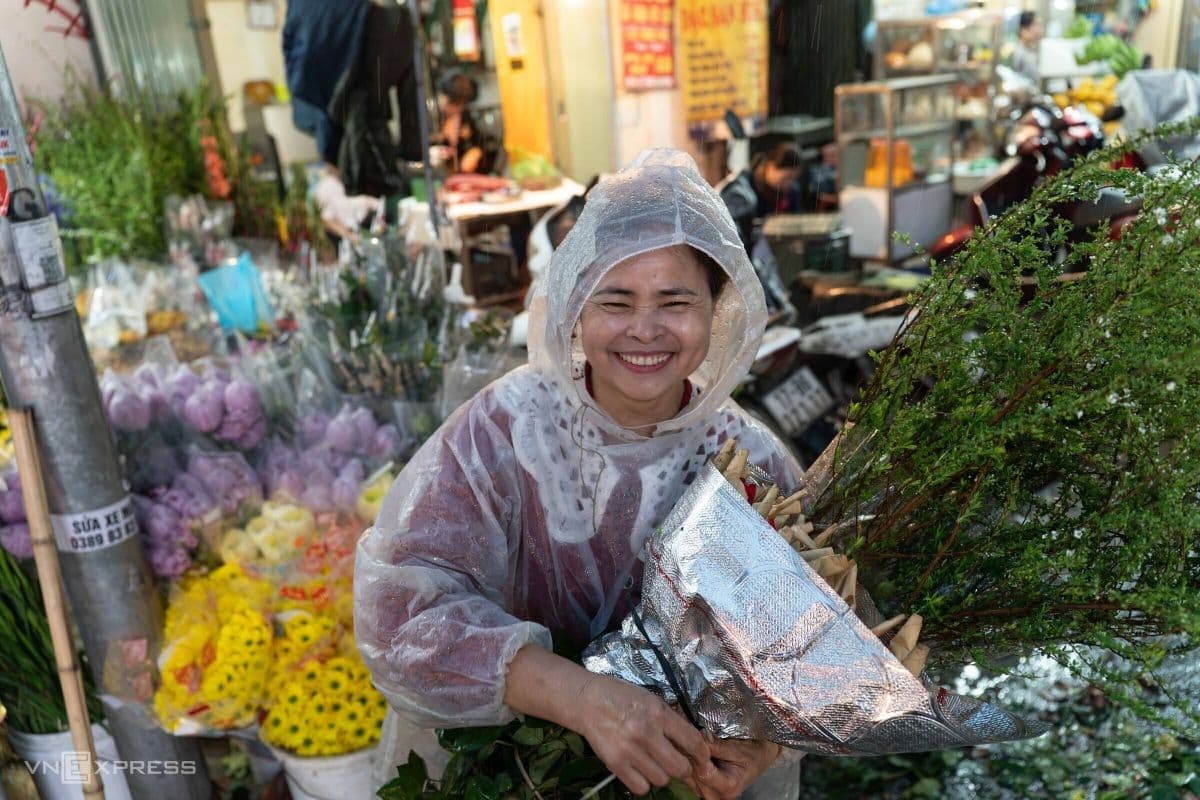 Người phụ nữ tươi cười chọn hoa tươi tại chợ, chuẩn bị trang trí cho bàn thờ sau khi bao sái, mang lại không gian thanh tịnh và đẹp đẽ.