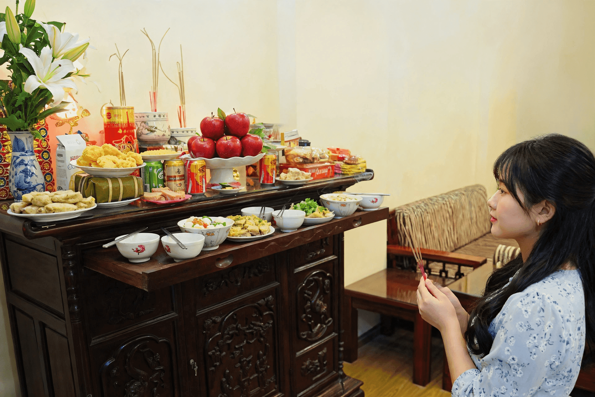 Người phụ nữ trẻ mặc áo sáng màu đang khấn vái trước bàn thờ đầy đủ lễ vật, tượng trưng cho sự giao thoa giữa truyền thống và hiện đại trong nghi lễ mùng 1 tháng 6.
