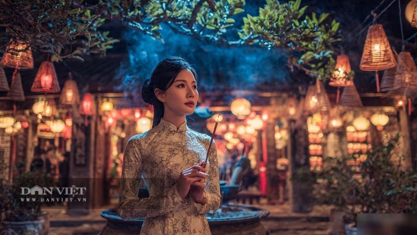 Người phụ nữ Việt Nam trong áo dài truyền thống thắp hương trong không gian thờ cúng lung linh ánh đèn, thể hiện nghi lễ Rằm.