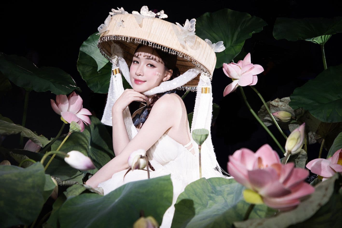 Người phụ nữ Việt Nam trong trang phục trắng và nón vành, giữa những bông sen hồng.