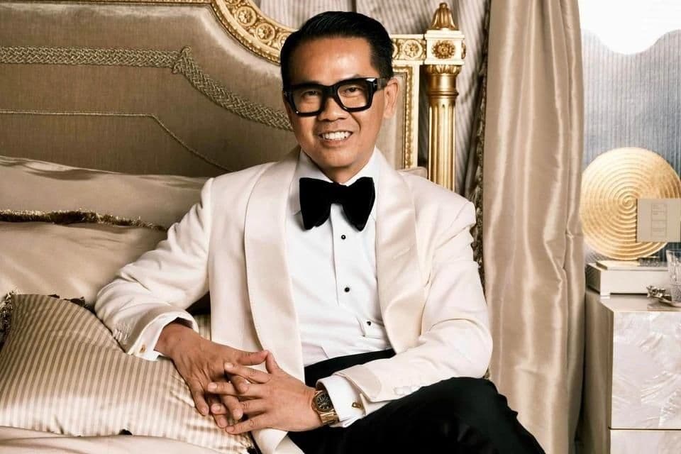 Nhà thiết kế nội thất Quách Thái Công trong bộ tuxedo trắng sang trọng, ngồi trên giường với phong cách xa hoa.
