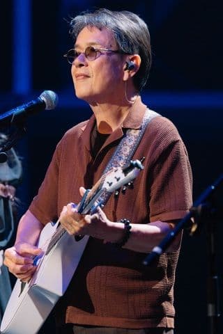 Nhạc sĩ Đức Huy biểu diễn trên sân khấu với cây đàn guitar, thể hiện phong độ ở tuổi U80.