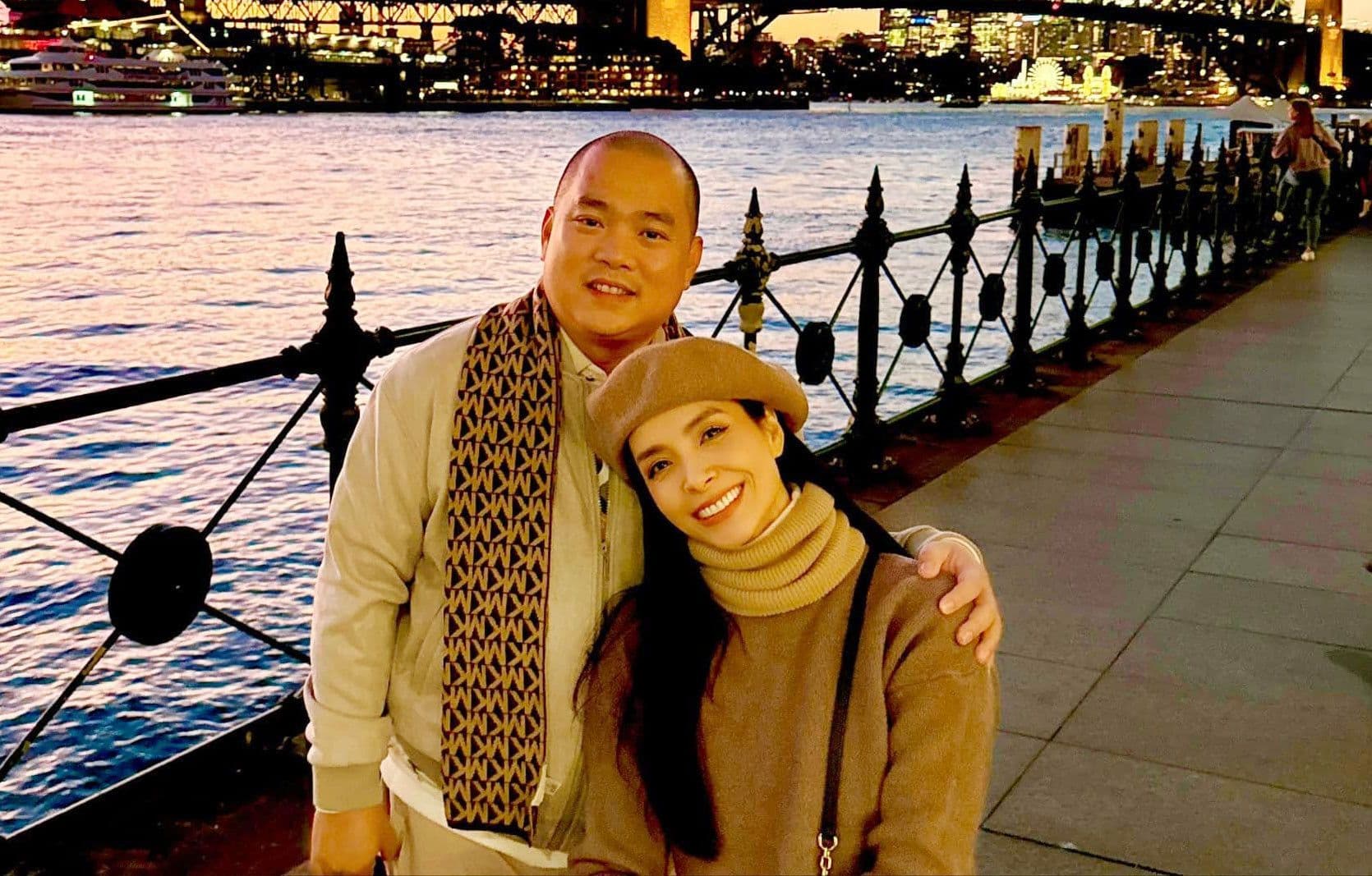 Nhạc sĩ Minh Khang và vợ Thúy Hạnh tươi cười trong khung cảnh thành phố lãng mạn, đại diện cho hình ảnh công chúng hoàn hảo của họ.