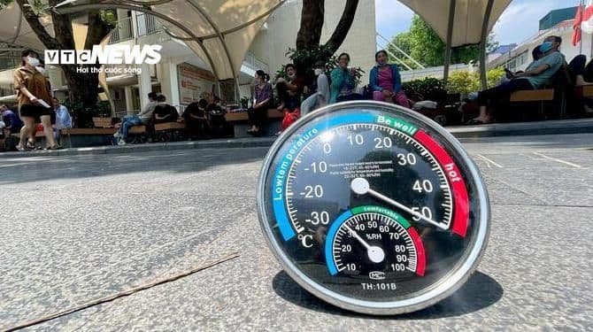 Nhiệt kế ngoài trời hiển thị nhiệt độ cao trong ngày nắng nóng ở Hà Nội, với người dân tìm bóng râm phía sau.