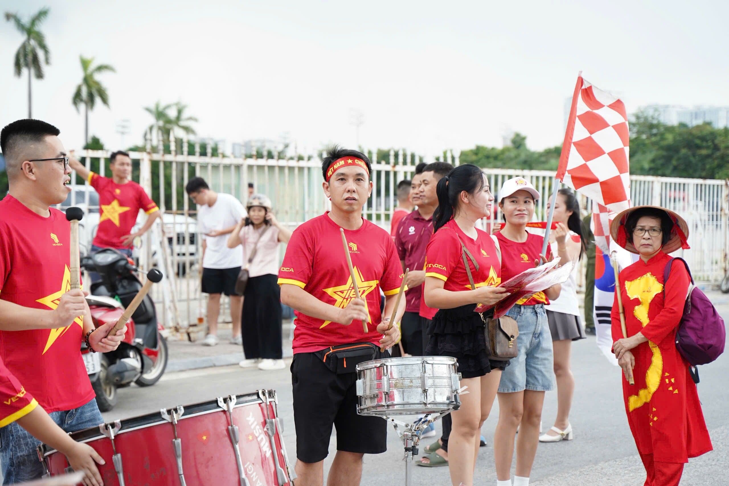 Nhóm cổ động viên Việt Nam mặc áo đỏ sao vàng, đánh trống và vẫy cờ, thể hiện tinh thần cộng đồng hâm mộ bóng đá.