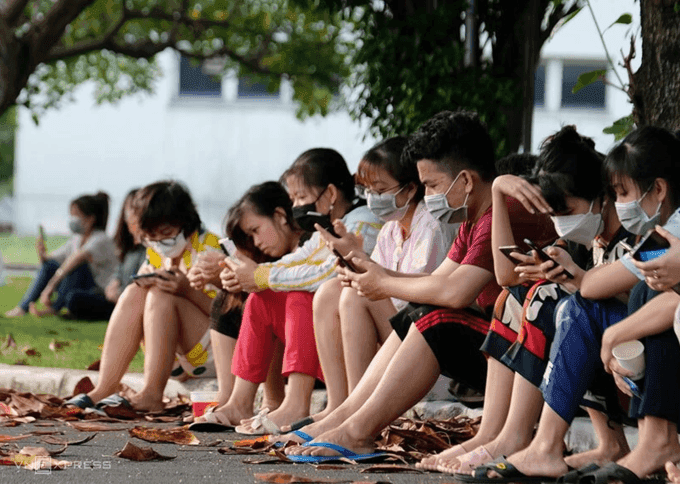 Nhóm công nhân trẻ ngồi nghỉ, sử dụng điện thoại, thể hiện cuộc sống và nỗi lo của người lao động Việt Nam.