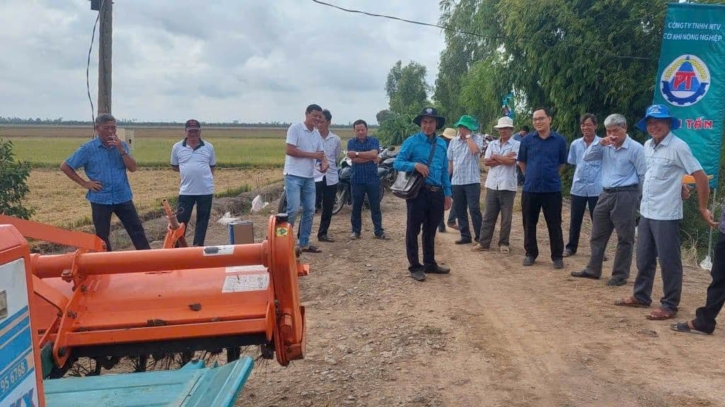 Nhóm nông dân và cán bộ đứng cạnh máy cày trên cánh đồng, thể hiện sự chuyển đổi và hiện đại hóa nông nghiệp Việt Nam.