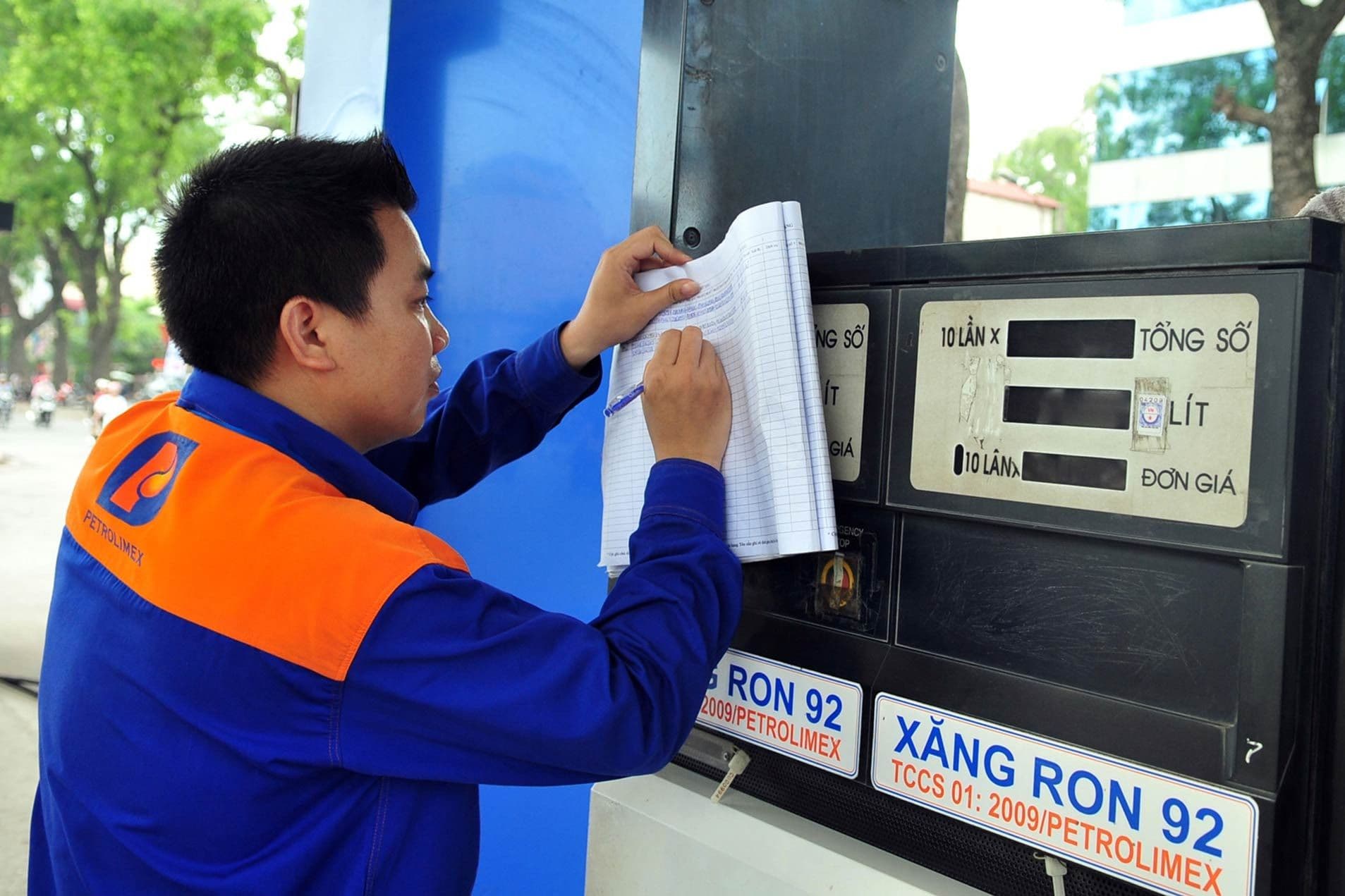 Nhân viên cây xăng ghi chép thông tin tại trụ bơm, liên quan đến việc điều chỉnh giá xăng dầu.