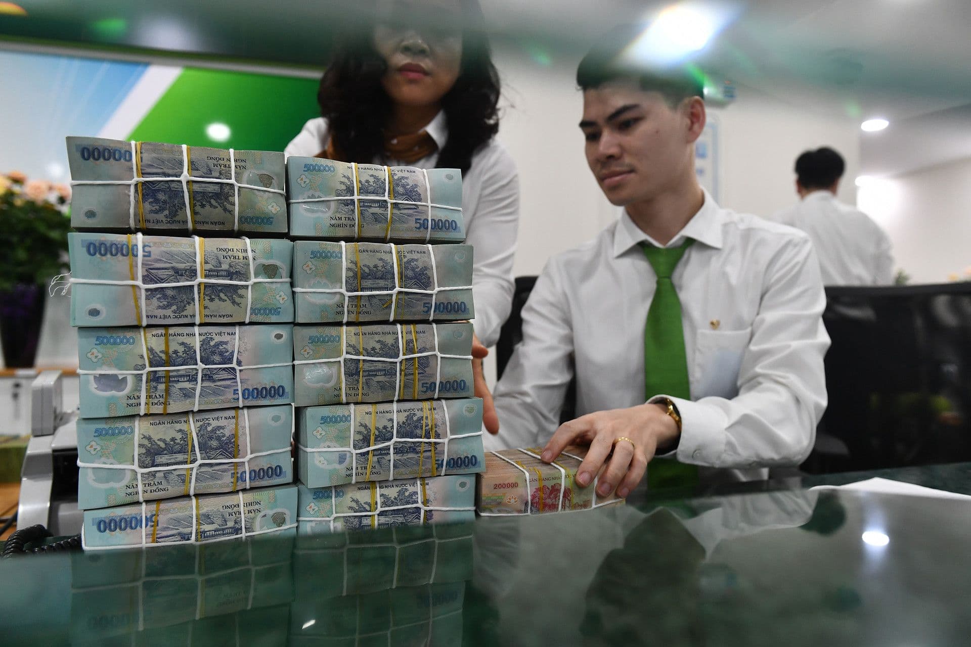 Nhân viên ngân hàng Việt Nam đang sắp xếp chồng tiền mệnh giá 500.000 VND, tượng trưng cho dòng vốn và gánh nặng tài chính.