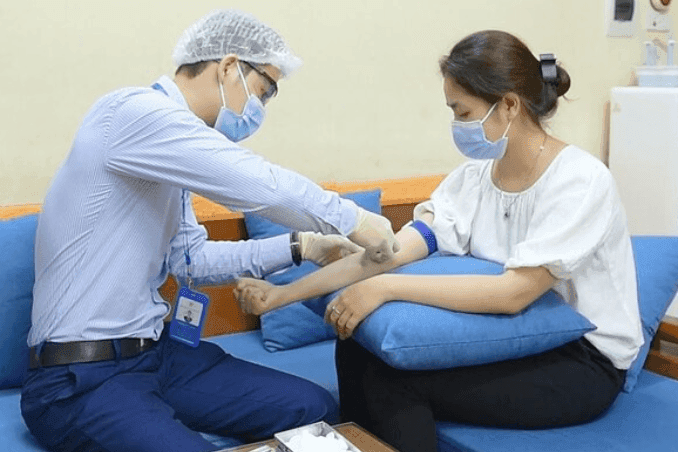 Nhân viên y tế lấy mẫu máu từ bệnh nhân, tượng trưng cho việc xét nghiệm, tiêm chủng và theo dõi miễn dịch cộng đồng