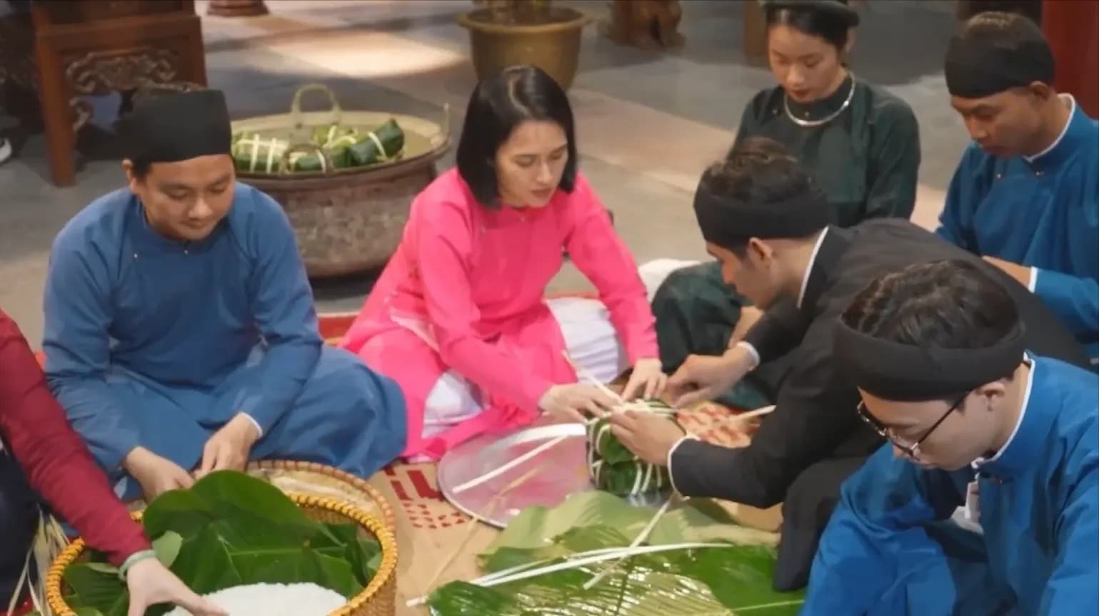 Những người Việt mặc áo truyền thống đang tỉ mỉ gói bánh chưng bằng lá dong và gạo nếp, thể hiện sự khéo léo và truyền thống.