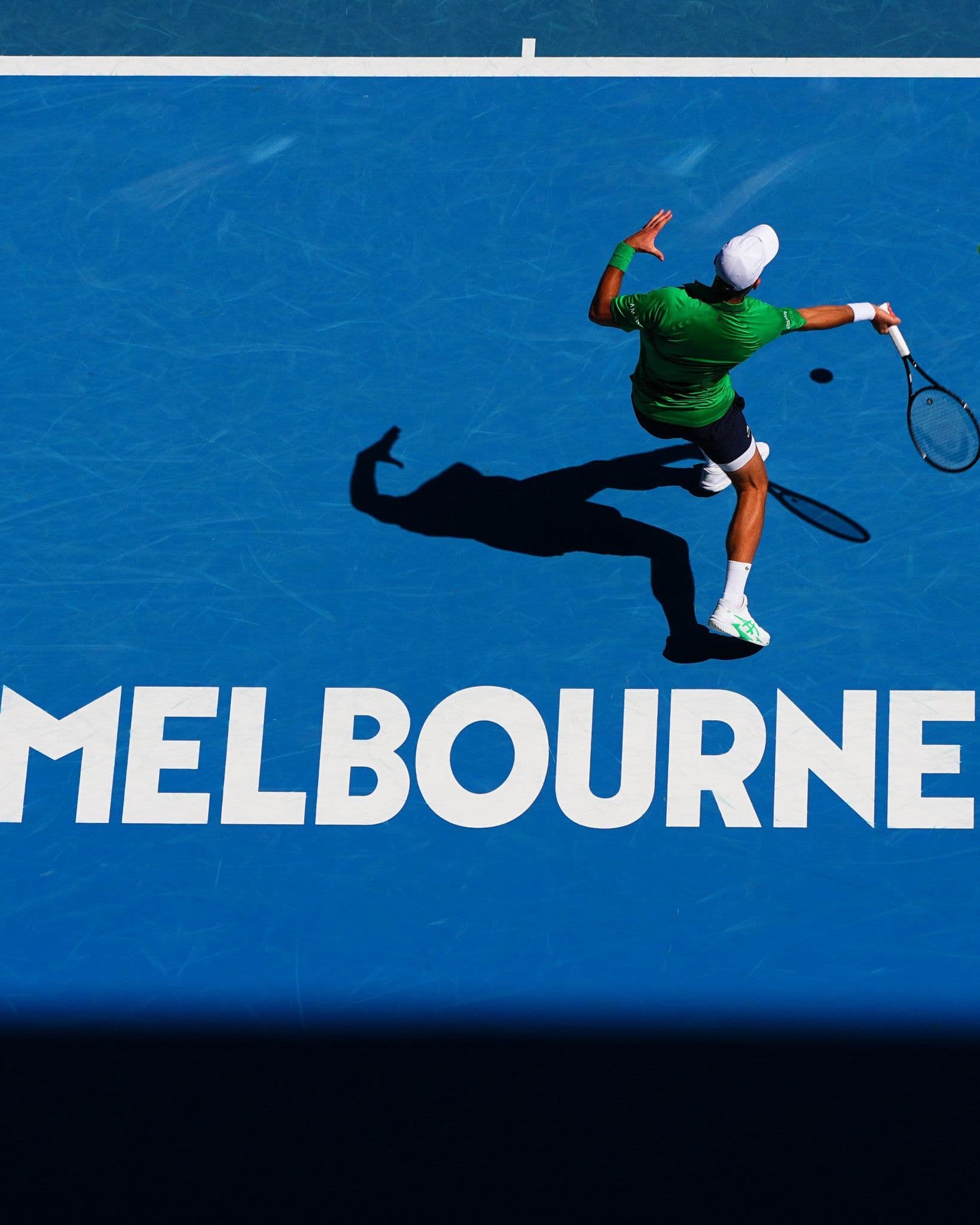 Novak Djokovic đánh bóng trên sân xanh với chữ 'Melbourne' tại Australian Open