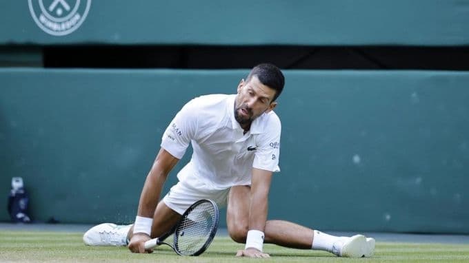 Novak Djokovic trượt ngã trên sân cỏ Wimbledon, tượng trưng cho áp lực và những thách thức anh đang đối mặt.