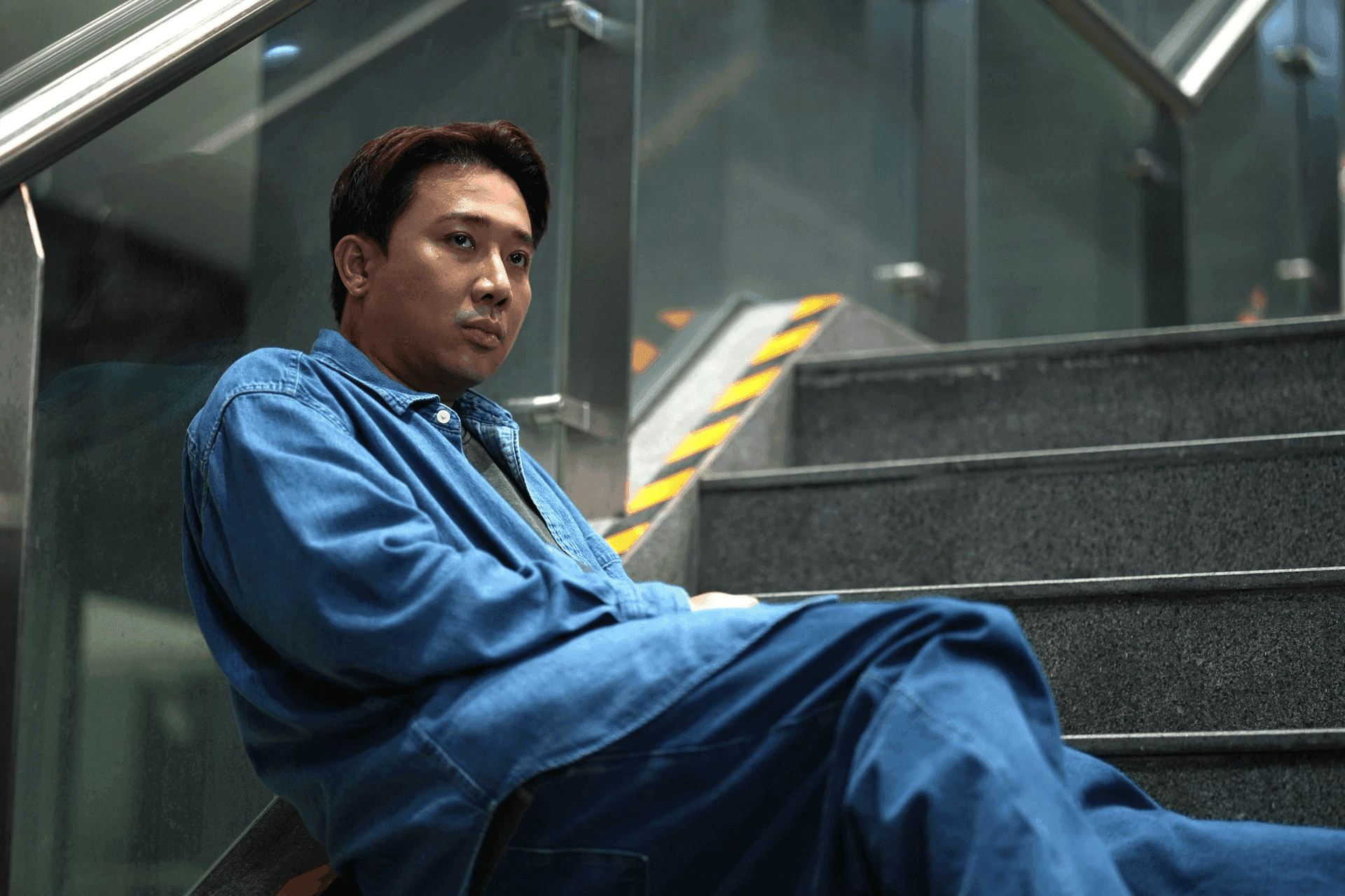 Đạo diễn Trấn Thành ngồi trầm tư trên cầu thang, thể hiện sự lo lắng trước vấn nạn spoiler và đạo đức khán giả