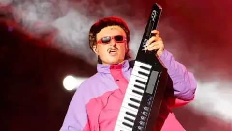 Oliver Tree biểu diễn trên sân khấu với kiểu tóc bát úp đặc trưng, đeo kính râm và chơi đàn keytar, thể hiện phong cách độc đáo của anh.
