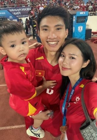 Đoàn Văn Hậu, vợ Doãn Hải My và con trai trên sân cỏ sau chiến thắng, tất cả mặc áo đấu màu đỏ.