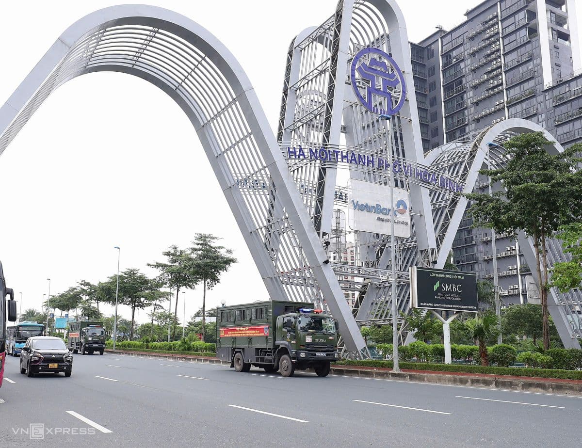 Đoàn xe quân sự di chuyển trên đường phố Hà Nội, phía sau là cổng chào lớn, thể hiện sự chuẩn bị cho diễu binh.