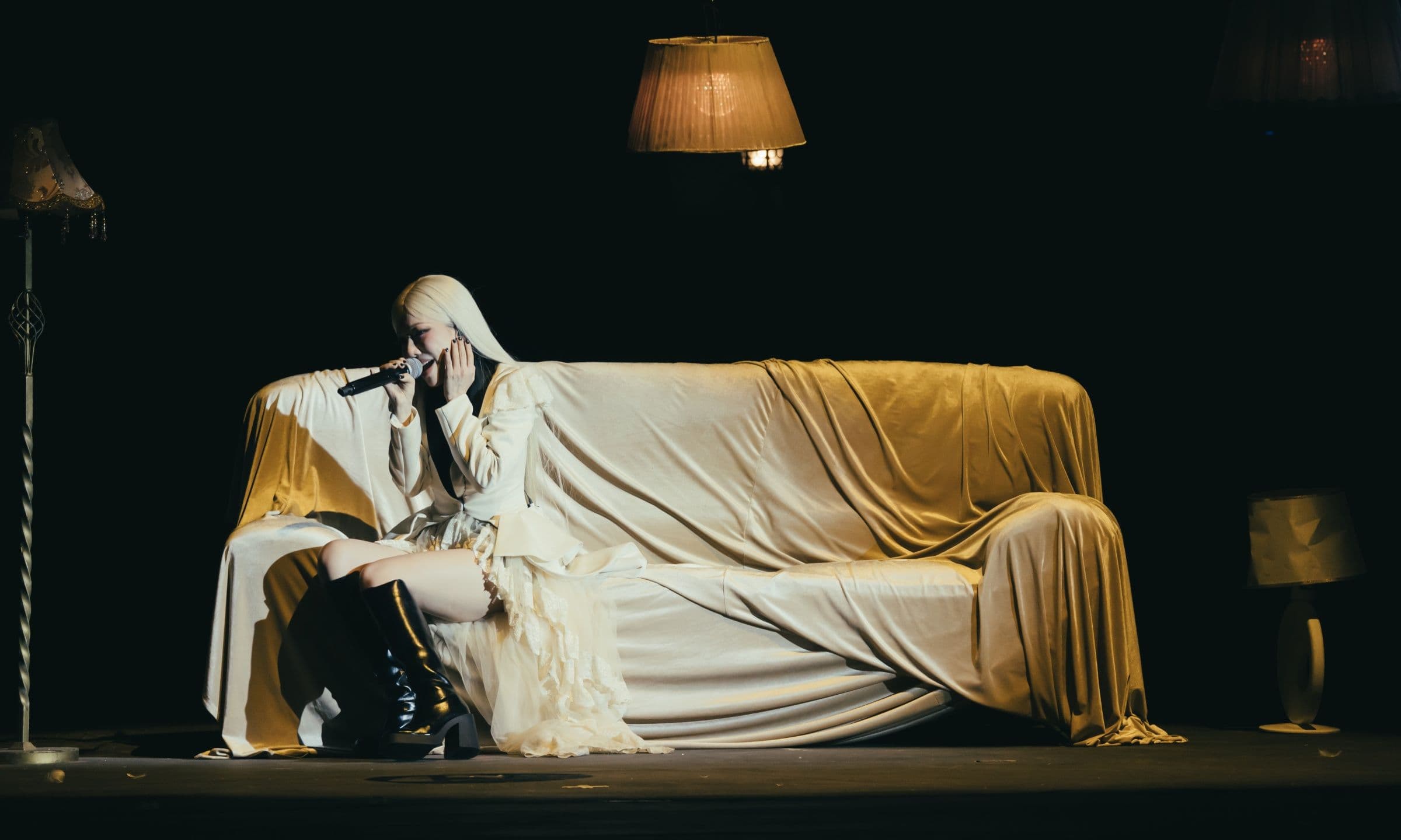 Phùng Khánh Linh ngồi trên ghế sofa trên sân khấu, thể hiện những ca khúc đầy cảm xúc từ nỗi buồn và hoài nghi.