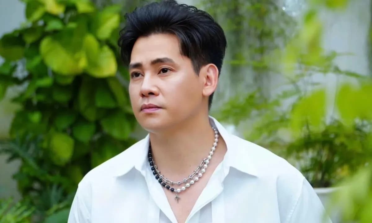 Phùng Ngọc Huy với vẻ mặt trầm tư, mặc áo sơ mi trắng và đeo vòng cổ, đứng giữa không gian xanh mát, thể hiện sự bình yên và tĩnh lặng.