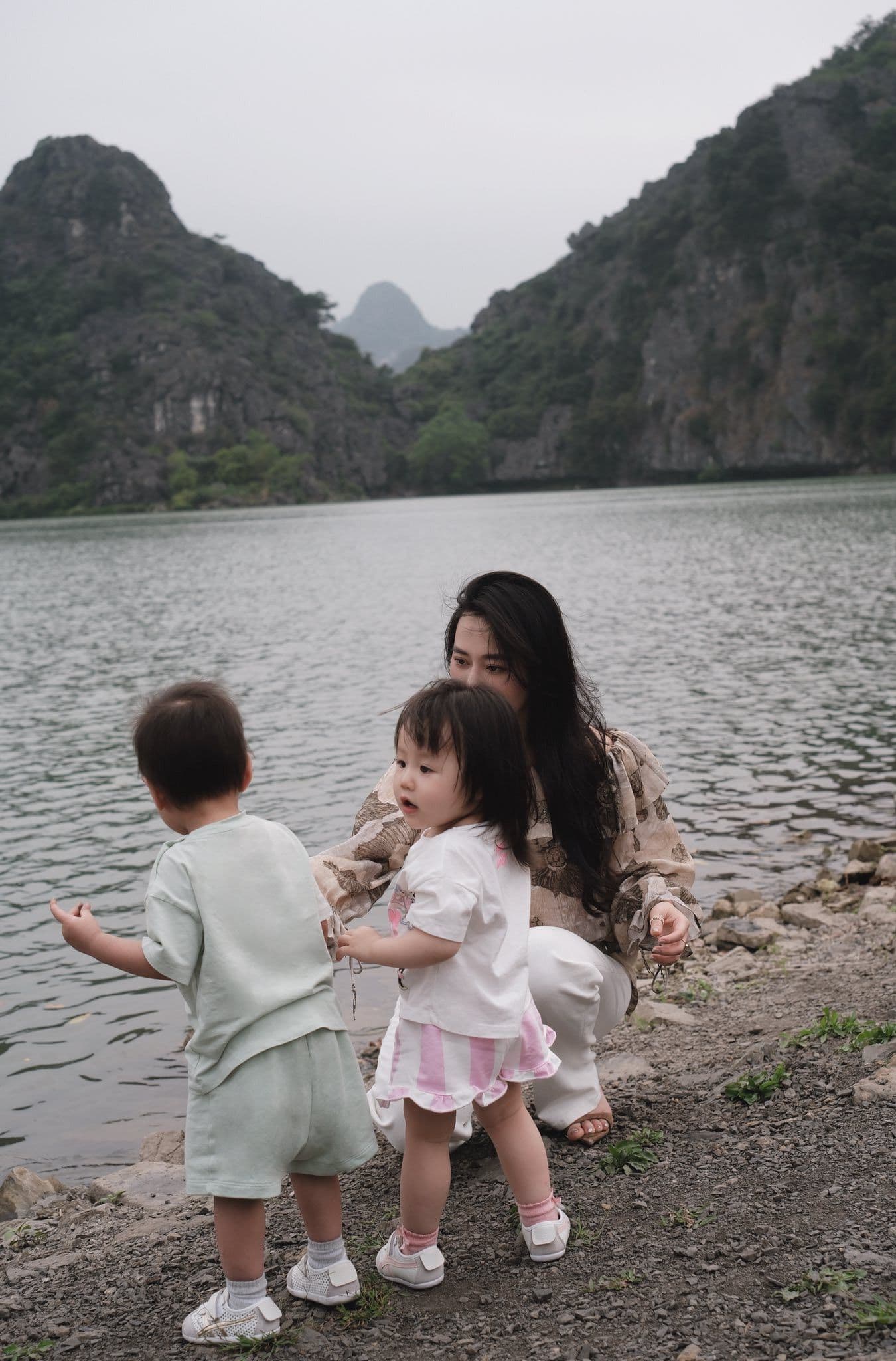 Phương Oanh vui vẻ chơi đùa cùng hai con nhỏ bên bờ hồ, thể hiện sự bình yên và hạnh phúc gia đình.