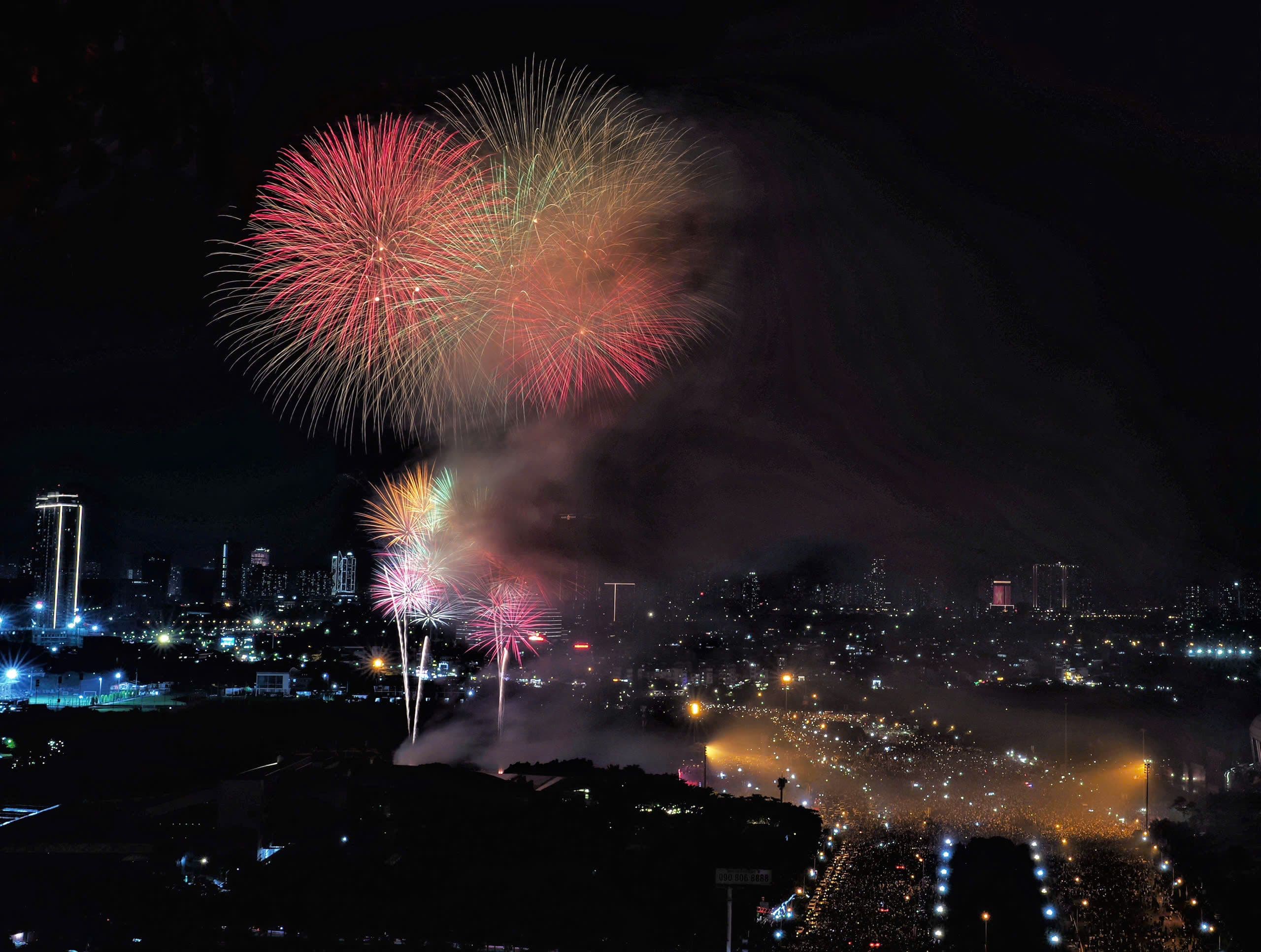 Pháo hoa rực rỡ thắp sáng bầu trời đêm Quốc khánh 2/9 trên nền thành phố và dòng người đông đúc.