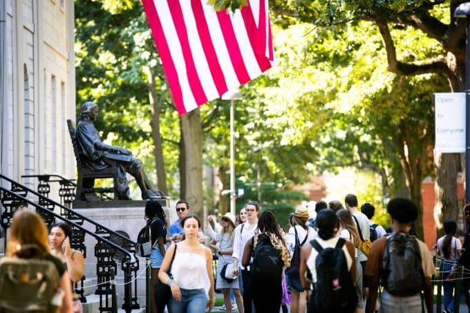 Sinh viên đi bộ qua tượng đài John Harvard tại khuôn viên Đại học Harvard, biểu tượng của giáo dục tinh hoa đang đối mặt với thách thức.