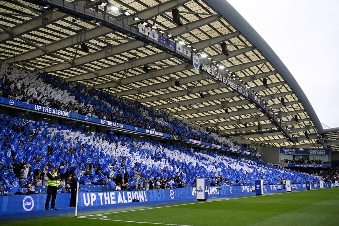 Sân vận động American Express với hàng ngàn người hâm mộ vẫy cờ, tượng trưng cho khán đài toàn cầu của bóng đá trực tiếp.