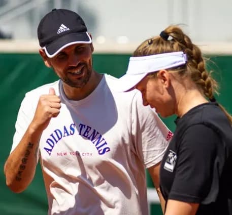 Stefano Vukov tươi cười trong khi Elena Rybakina cúi mặt, thể hiện sự đối lập trong mối quan hệ.