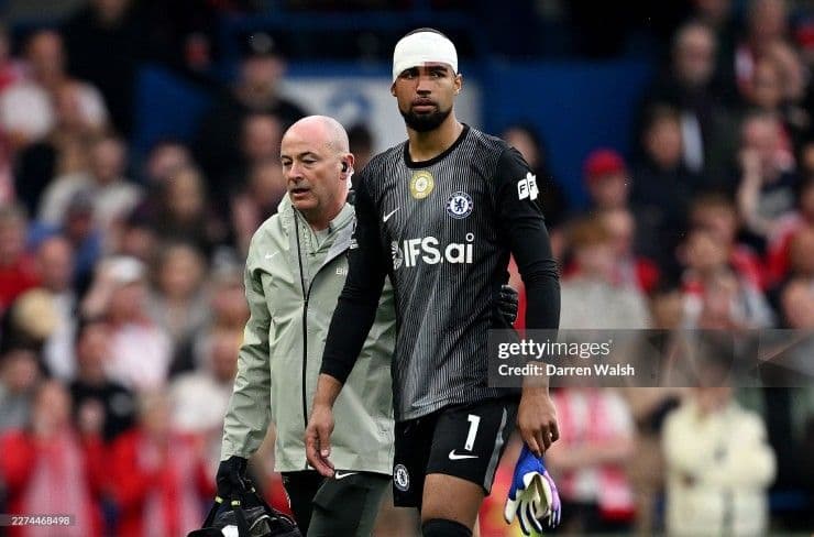 Thủ môn Chelsea với băng quấn đầu được hỗ trợ rời sân, biểu tượng cho những 'vết nứt' và sự rệu rã trong cấu trúc đội bóng.