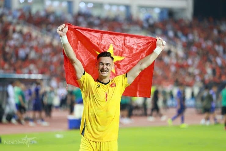 Thủ môn Patrik Lê Giang mặc áo vàng, giơ cao cờ Việt Nam sau khi nhận cúp, hình ảnh được MC Hoàng Oanh cổ vũ.