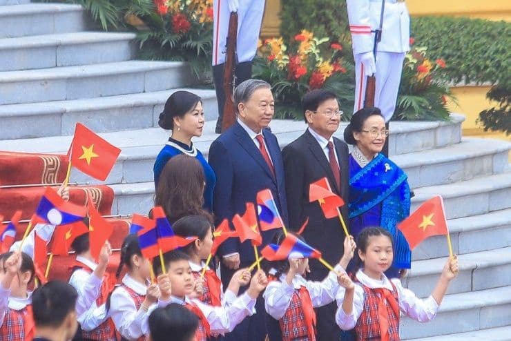 Tổng Bí thư Tô Lâm và Phu nhân cùng Tổng Bí thư, Chủ tịch nước Lào Thongloun Sisoulith và Phu nhân vẫy tay chào trẻ em cầm cờ Việt-Lào, biểu tượng tình hữu nghị.