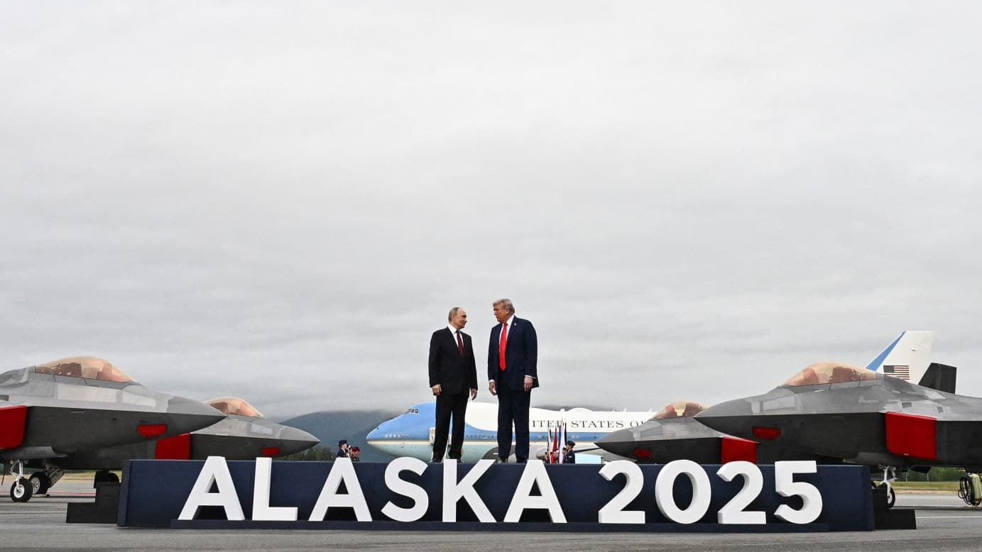 Tổng thống Donald Trump và Vladimir Putin đứng trên thảm đỏ ở Alaska, với máy bay chiến đấu và khẩu hiệu 'ALASKA 2025' phía sau, tượng trưng cho hội nghị thượng đỉnh.
