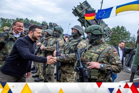Tổng thống Zelensky bắt tay binh sĩ Ukraine bên cạnh hệ thống phòng không Patriot và cờ các đồng minh, tượng trưng cho các liên minh địa chính trị.