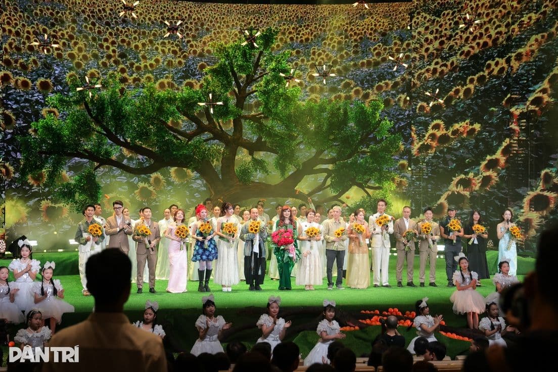 Toàn cảnh sân khấu True Concert Tình đất với dàn nghệ sĩ và trẻ em biểu diễn trước phông nền cây cổ thụ và cánh đồng hoa hướng dương rực rỡ