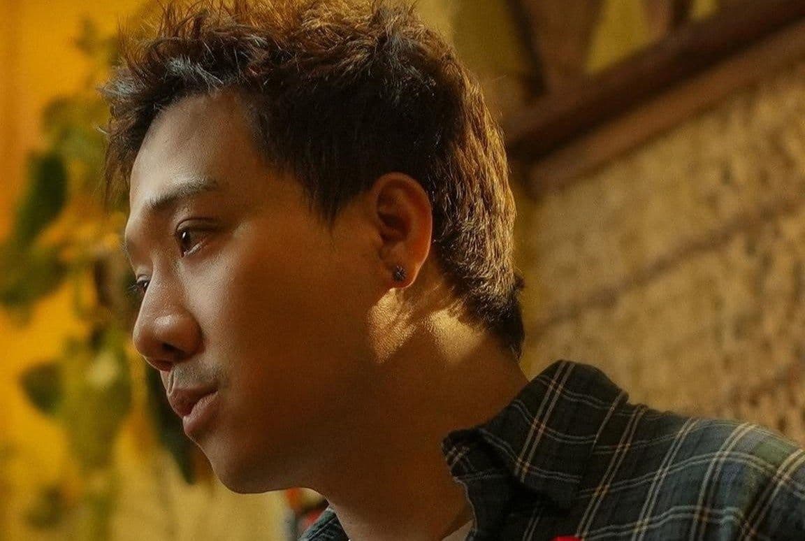 Trấn Thành nhìn nghiêng, thể hiện sự suy tư hoặc lắng nghe, phù hợp với việc tương tác trực tiếp với khán giả