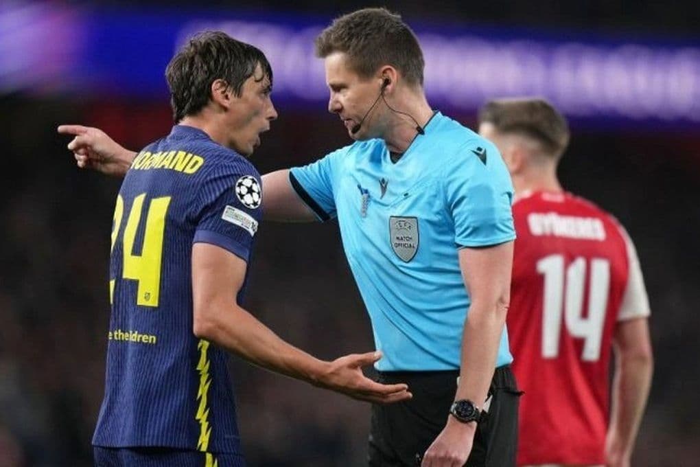 Trọng tài đang trao đổi với cầu thủ Dortmund, phía sau là cầu thủ Arsenal, thể hiện sự căng thẳng và tranh cãi trong trận đấu bóng đá.