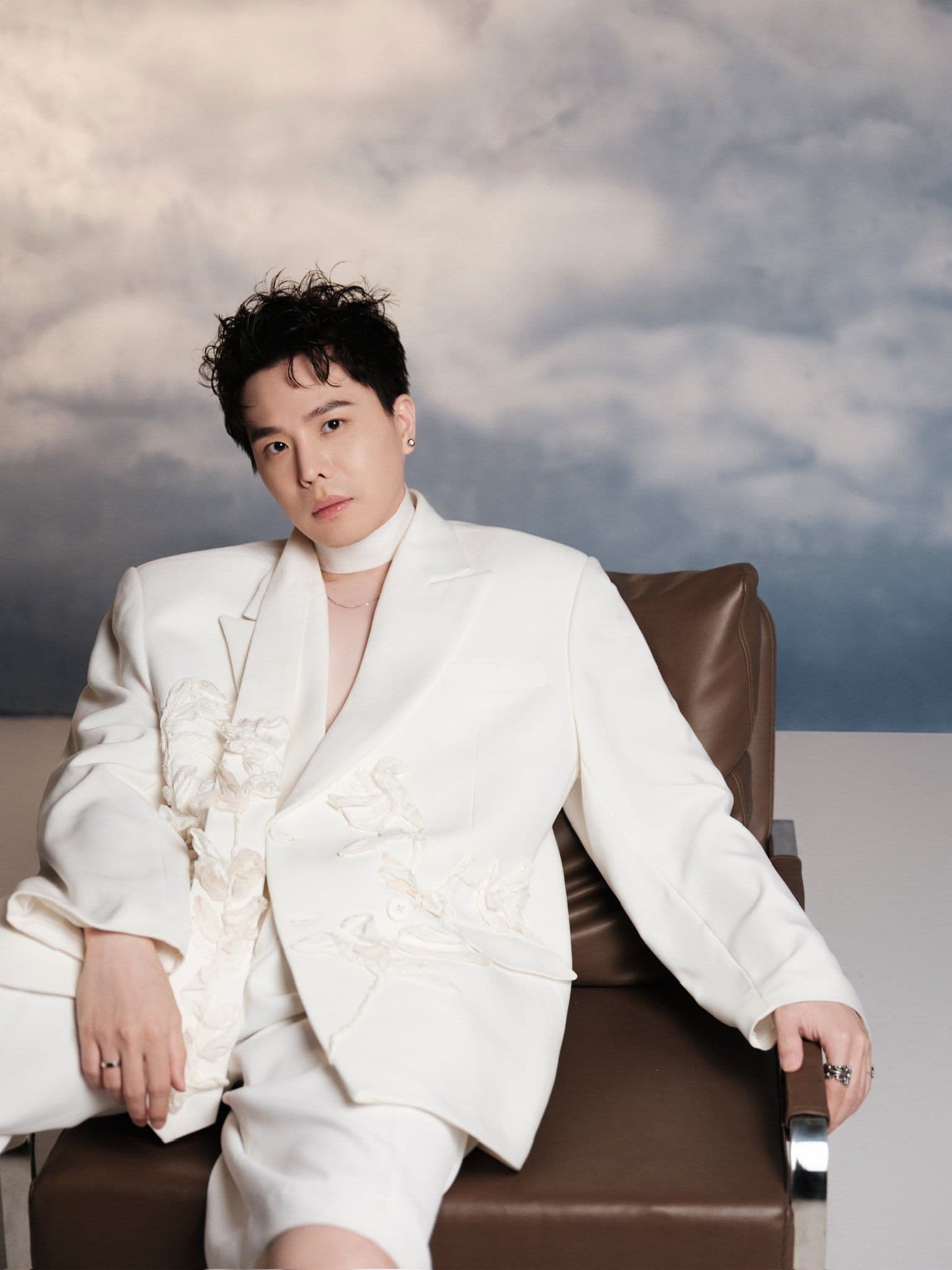 Trịnh Thăng Bình ngồi trầm tư trong bộ vest trắng, thể hiện sự bình yên và định nghĩa hạnh phúc riêng.