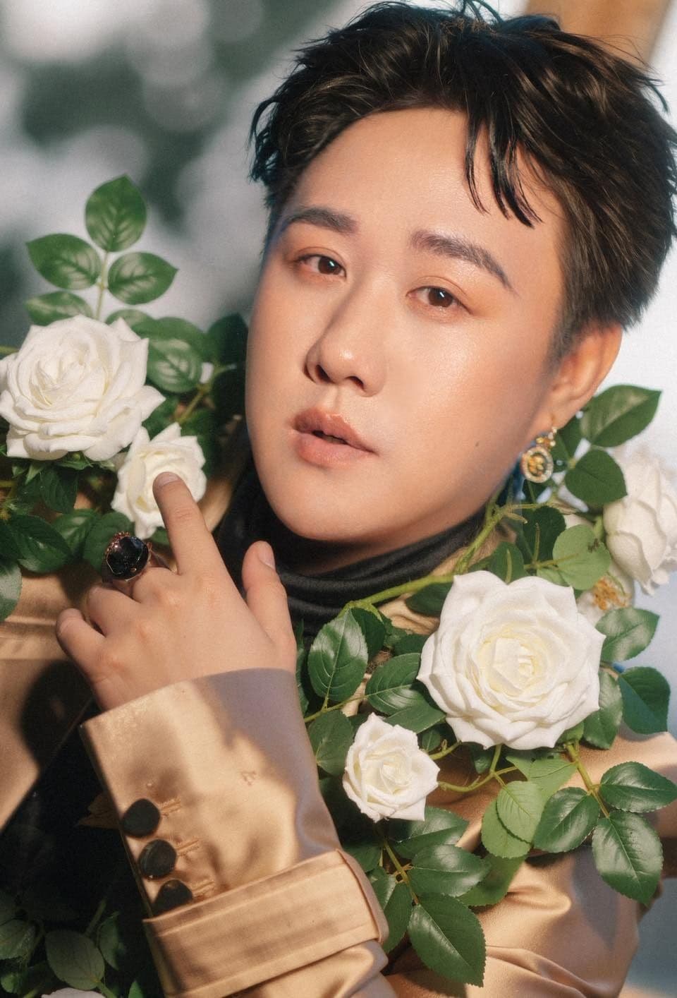 Trung Quân Idol trong trang phục vàng với hoa hồng trắng, thể hiện sự phức tạp của hào quang nghệ sĩ